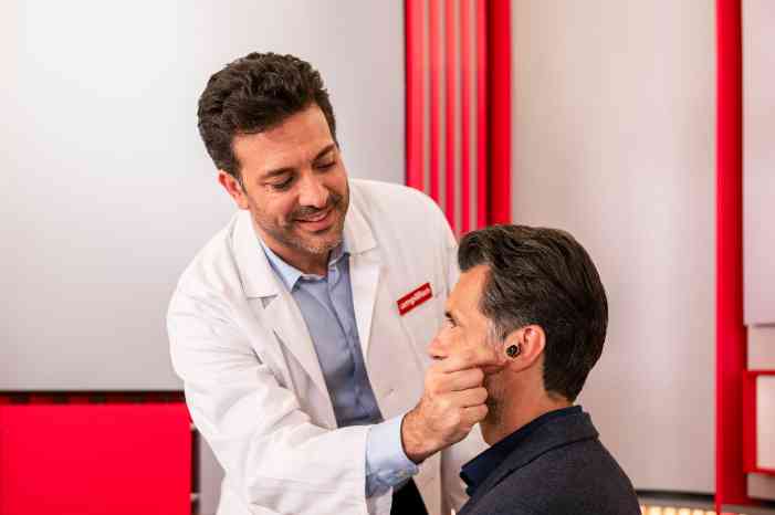 Audiologist fitting a hearing aid in client’s left ear