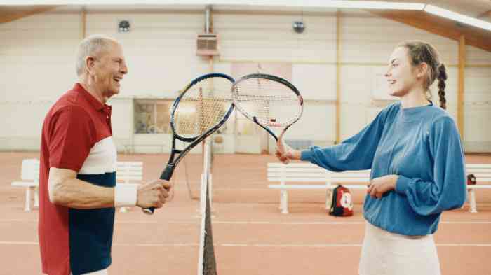 Opa met hoortoestel aan het tennissen met kleindochter